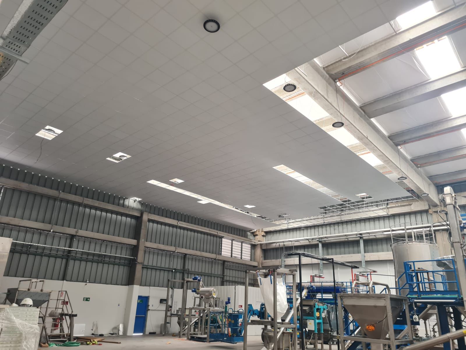 Nave industrial con cielo modular blanco e iluminación LED lineal entre las cerchas