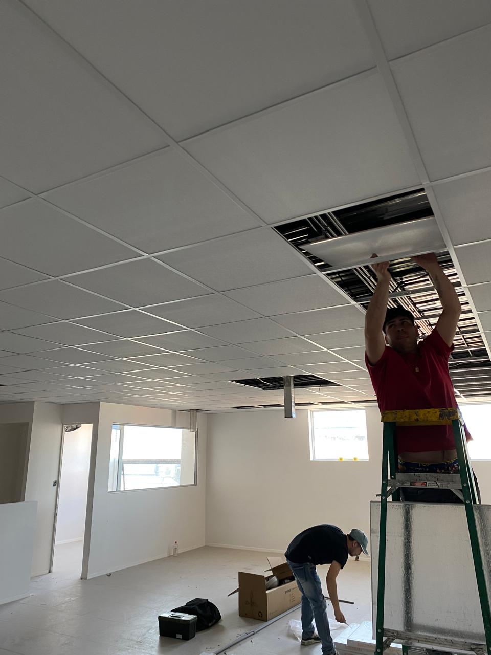 Instalador colocando placas de cielo americano desde una escalera