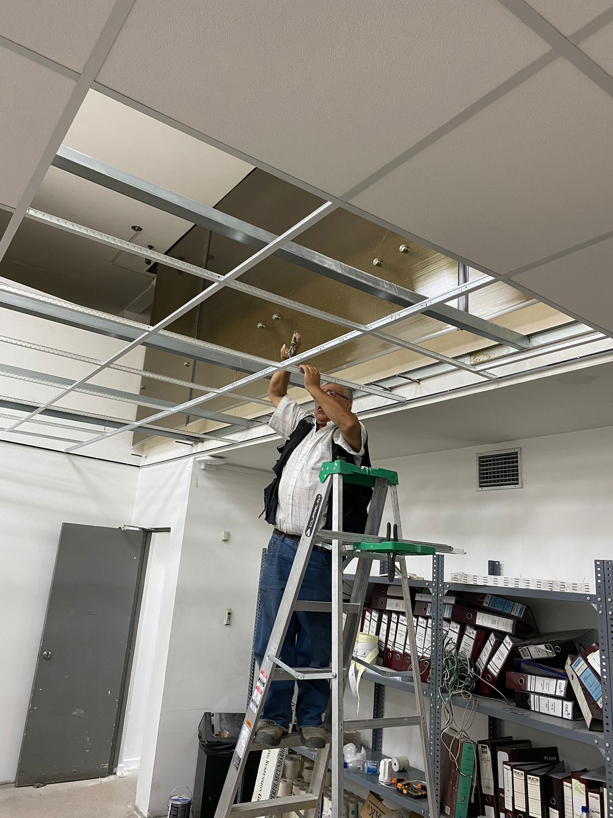 Instalador sobre escalera montando el cielo de una oficina