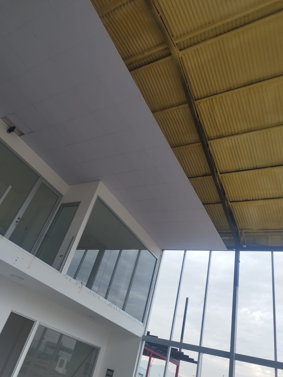 Cielo modular junto a estructura metálica amarilla y vidrio
